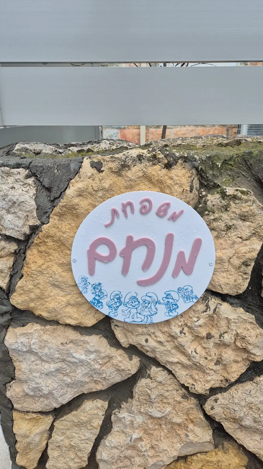 שלט כניסה לבן עם כיתוב ורוד ודרדסים, על קיר אבן